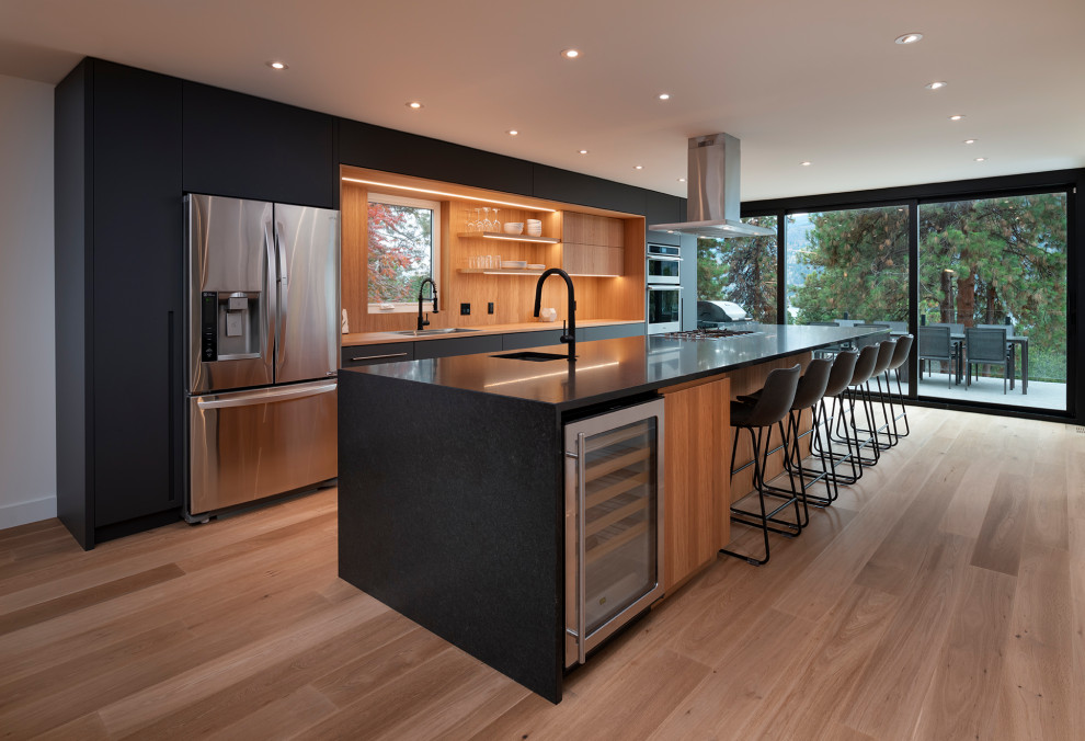 This is an example of a contemporary galley kitchen in Vancouver with an undermount sink, flat-panel cabinets, black cabinets, brown splashback, timber splashback, stainless steel appliances, medium hardwood floors, with island, brown floor and black benchtop.