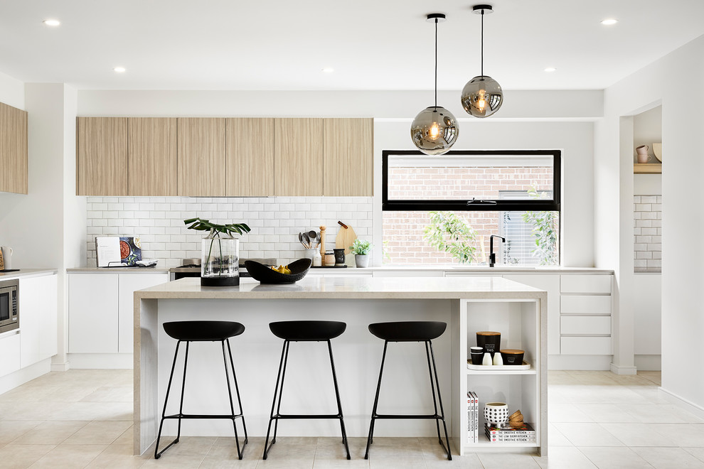 This is an example of a modern l-shaped kitchen in Melbourne with an undermount sink, flat-panel cabinets, light wood cabinets, white splashback, subway tile splashback, stainless steel appliances, with island, beige floor and beige benchtop.