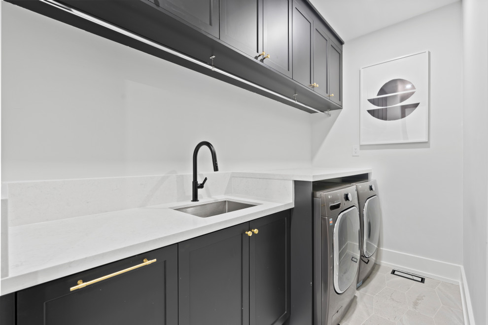 Contemporary galley utility room in Toronto with a submerged sink, shaker cabinets, engineered stone countertops, white splashback, white walls, porcelain flooring, a side by side washer and dryer, grey floors and white worktops.