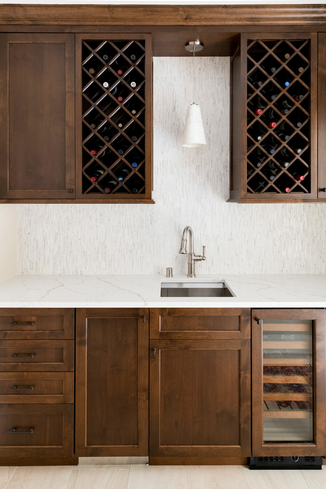 Photo of a small arts and crafts galley wet bar in Minneapolis with a drop-in sink, flat-panel cabinets, medium wood cabinets, quartz benchtops, white splashback, mosaic tile splashback, ceramic floors, beige floor and white benchtop.