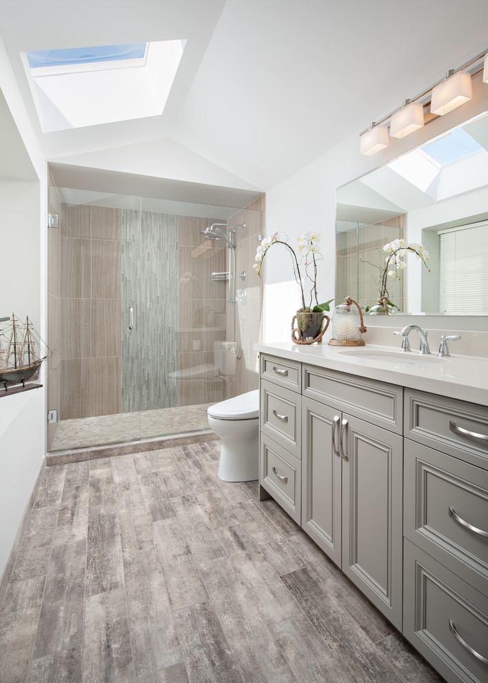 Inspiration for a mid-sized transitional master bathroom in Vancouver with an undermount sink, recessed-panel cabinets, grey cabinets, engineered quartz benchtops, an alcove shower, a bidet, gray tile, porcelain tile, porcelain floors, white walls, brown floor and a hinged shower door.