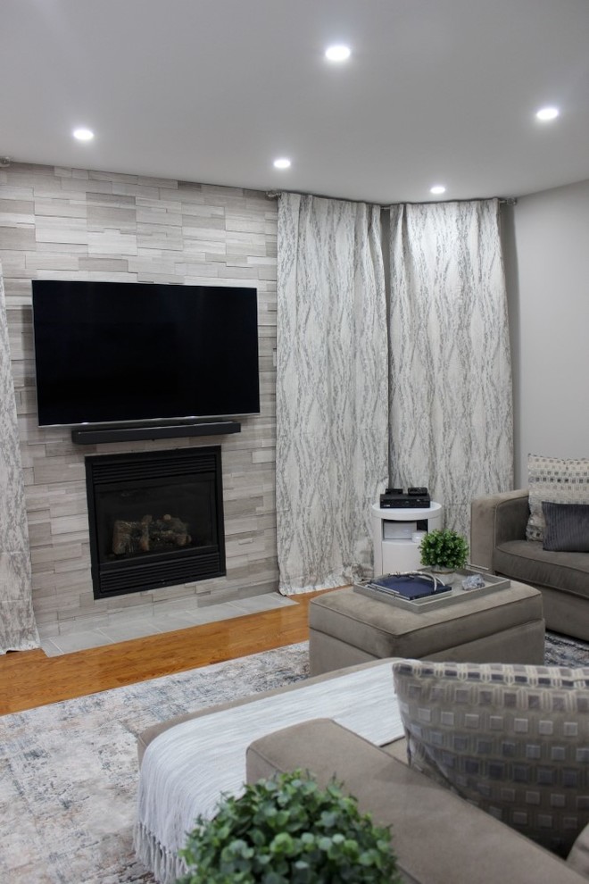 Mid-sized contemporary open concept family room in Toronto with grey walls, medium hardwood floors, a standard fireplace, a tile fireplace surround, a wall-mounted tv and brown floor.