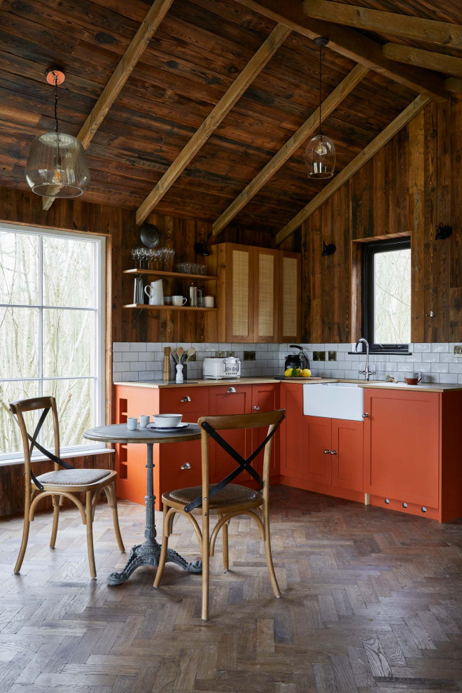 This is an example of a rustic l-shaped open plan kitchen in London with a belfast sink, shaker cabinets, orange cabinets, white splashback, metro tiled splashback, integrated appliances, dark hardwood flooring, no island, brown floors, beige worktops, exposed beams, a vaulted ceiling and a wood ceiling.