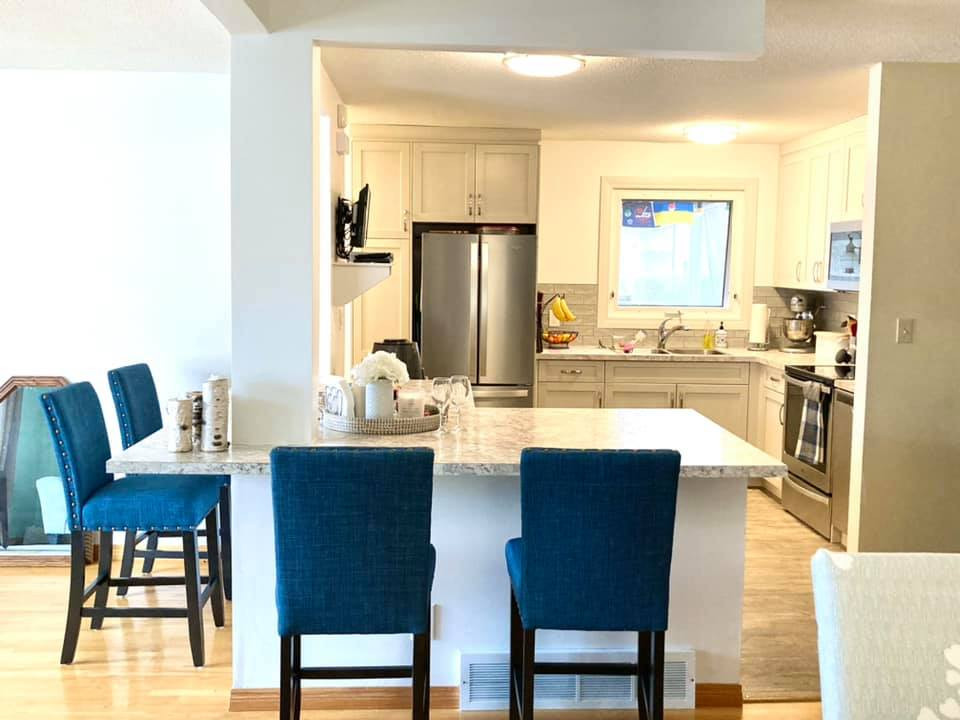 Mid-sized transitional l-shaped vinyl floor and beige floor open concept kitchen photo with a drop-in sink, shaker cabinets, beige cabinets, laminate countertops, gray backsplash, ceramic backsplash, stainless steel appliances, an island and multicolored countertops