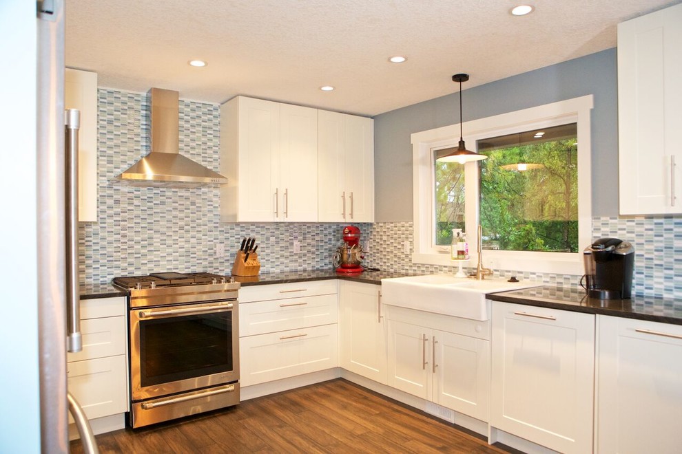 Inspiration for a mid-sized transitional u-shaped medium tone wood floor and brown floor enclosed kitchen remodel in Calgary with an undermount sink, shaker cabinets, white cabinets, solid surface countertops, blue backsplash, matchstick tile backsplash, stainless steel appliances and no island