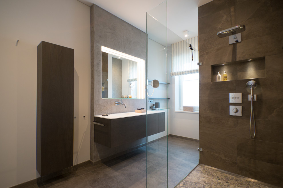 Duschbad With flächenbündigen Schrankfronten, braunen Schränken, bodengleicher Dusche, Wandtoilette, braunen Fliesen, Steinfliesen, weißer Wandfarbe, Mosaik-Bodenfliesen, integriertem Waschbecken and Mineralwerkstoff-Waschtisch in Berlin