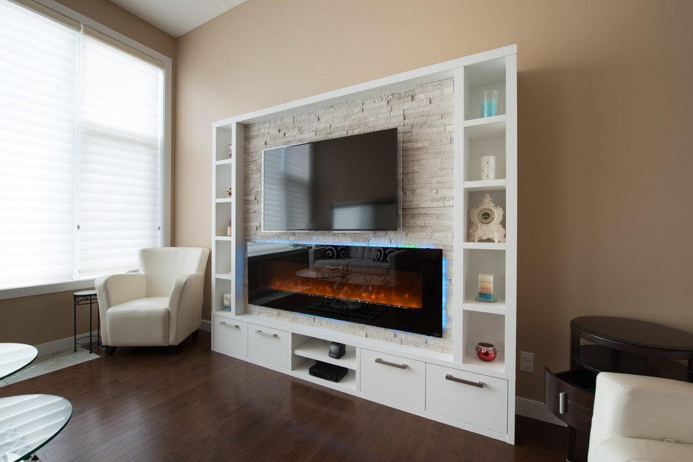 This is an example of a small modern open concept living room in Calgary with a library, beige walls, dark hardwood floors, a hanging fireplace, a stone fireplace surround and a built-in media wall.