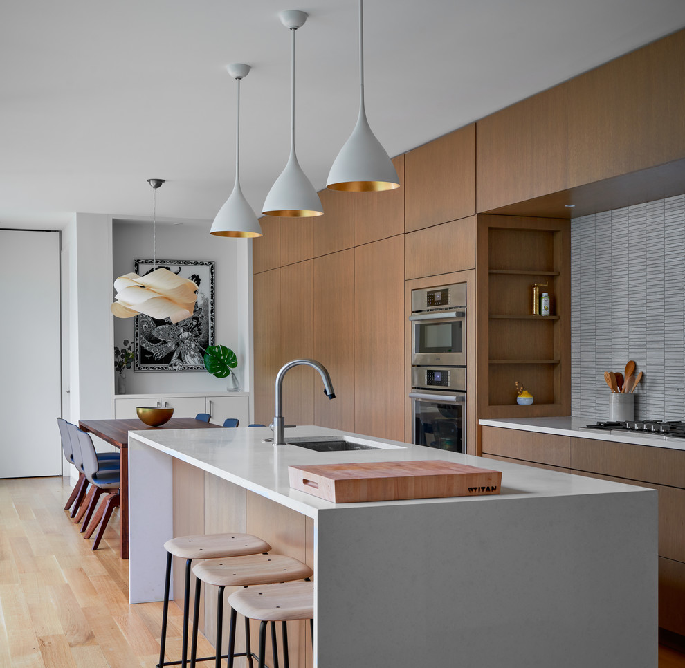 Design ideas for a contemporary galley eat-in kitchen in Austin with an undermount sink, flat-panel cabinets, white splashback, stainless steel appliances, light hardwood floors, with island, beige floor, white benchtop and medium wood cabinets.