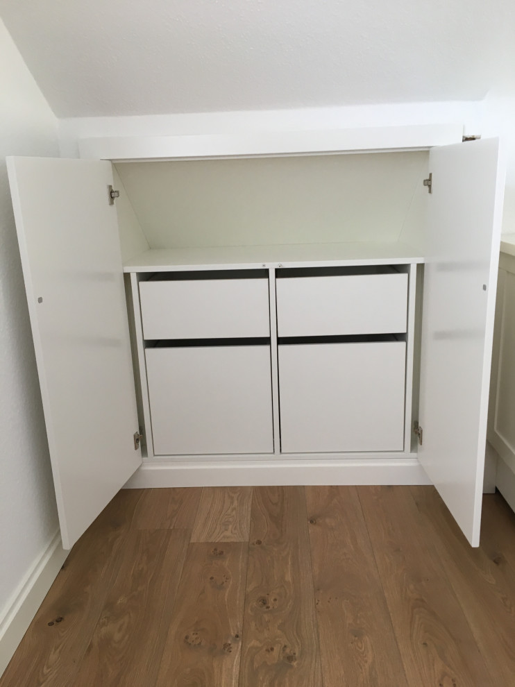 Imagen de armario y vestidor minimalista con puertas de armario blancas y suelo de madera en tonos medios
