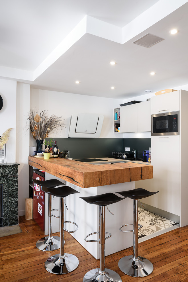 Inspiration for a small contemporary u-shaped kitchen in Lyon with flat-panel cabinets, beige cabinets, wood benchtops, black splashback, stainless steel appliances and a peninsula.