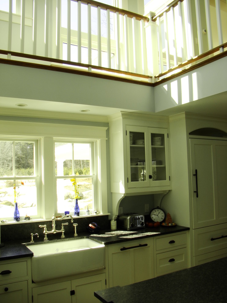 This is an example of a mid-sized traditional l-shaped open plan kitchen in Portland Maine with a farmhouse sink, beaded inset cabinets, white cabinets, granite benchtops, black splashback, stone slab splashback, panelled appliances, medium hardwood floors and with island.