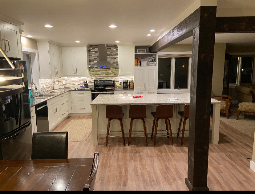 Example of a mid-sized transitional single-wall vinyl floor and multicolored floor eat-in kitchen design with an undermount sink, shaker cabinets, white cabinets, quartz countertops, multicolored backsplash, metal backsplash, black appliances, an island and white countertops