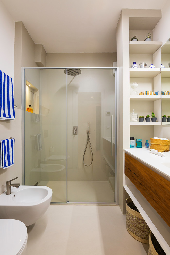 Photo of a small beach style 3/4 bathroom in Venice with flat-panel cabinets, dark wood cabinets, a curbless shower, beige tile, beige walls, solid surface benchtops, beige floor, a sliding shower screen, white benchtops and a bidet.