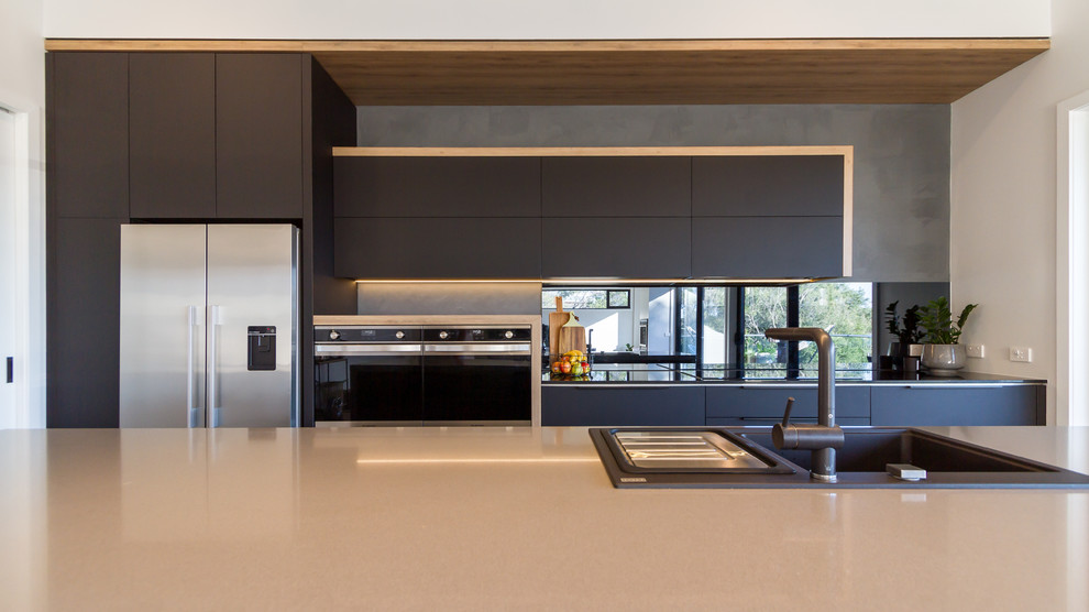 This is an example of a mid-sized modern galley eat-in kitchen in Melbourne with a drop-in sink, flat-panel cabinets, black cabinets, quartz benchtops, black splashback, mirror splashback, stainless steel appliances, light hardwood floors, with island, beige floor and grey benchtop.