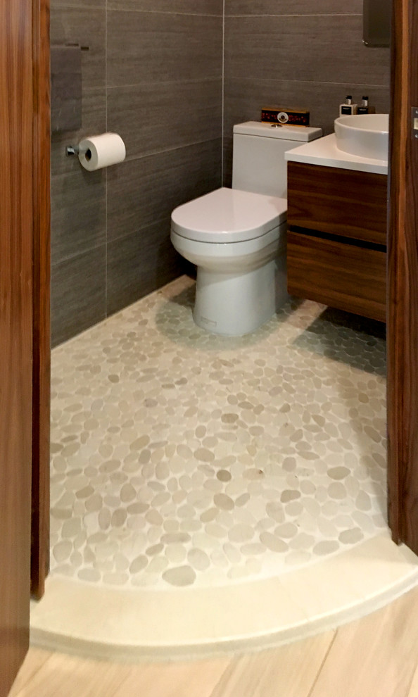Inspiration for a small modern powder room in New York with flat-panel cabinets, brown cabinets, a one-piece toilet, gray tile, porcelain tile, grey walls, pebble tile floors, a vessel sink, engineered quartz benchtops and multi-coloured floor.