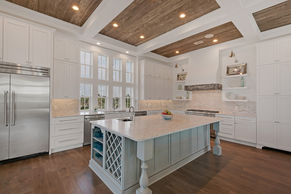Photo of an expansive beach style l-shaped open plan kitchen in Miami with a double-bowl sink, recessed-panel cabinets, white cabinets, marble benchtops, white splashback, stainless steel appliances, dark hardwood floors, with island, marble splashback and beige floor.