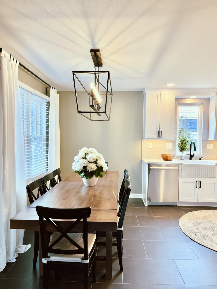Mid-sized transitional l-shaped vinyl floor and black floor eat-in kitchen photo with a farmhouse sink, shaker cabinets, white cabinets, quartz countertops, gray backsplash, ceramic backsplash, stainless steel appliances, a peninsula and gray countertops
