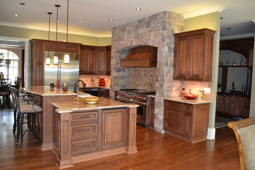 Example of a mid-sized mountain style l-shaped dark wood floor and brown floor eat-in kitchen design in Atlanta with a farmhouse sink, raised-panel cabinets, dark wood cabinets, granite countertops, beige backsplash, stone tile backsplash, stainless steel appliances and an island