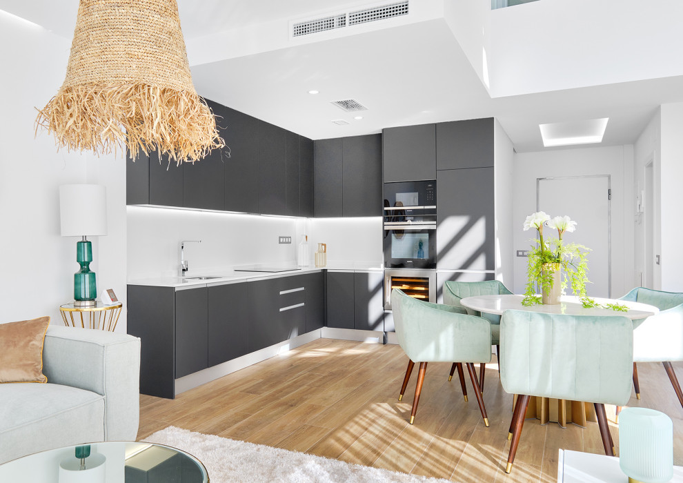Design ideas for a contemporary l-shaped kitchen in Alicante-Costa Blanca with an undermount sink, flat-panel cabinets, grey cabinets, black appliances, medium hardwood floors, brown floor and white benchtop.