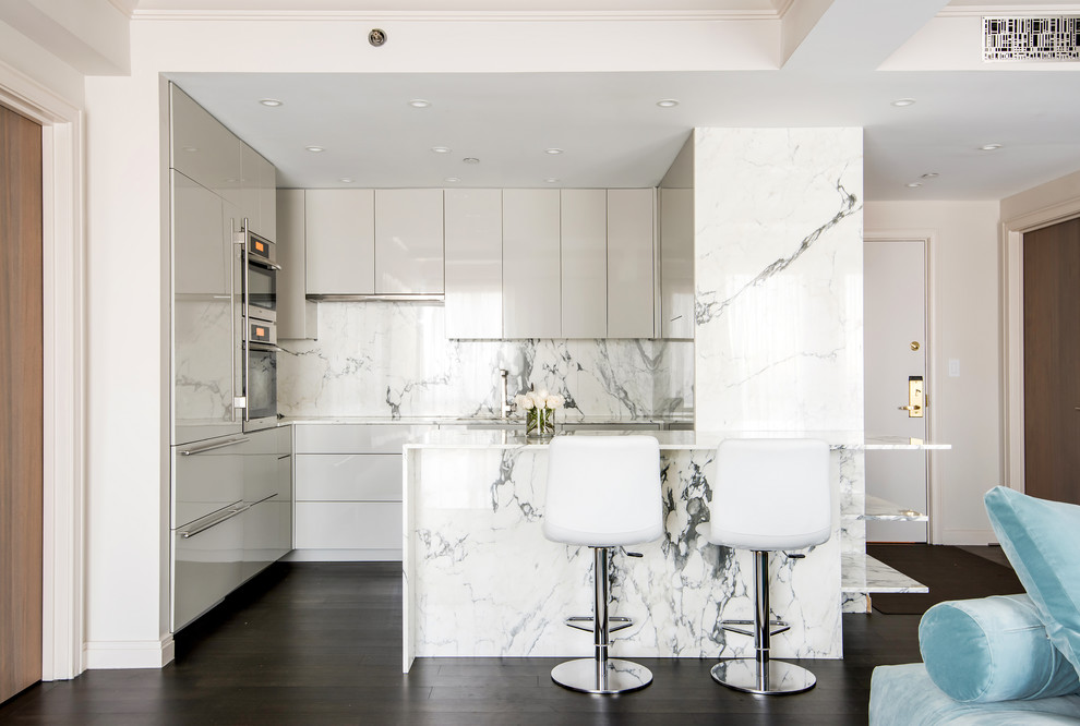 Inspiration for a mid-sized contemporary u-shaped kitchen in New York with an undermount sink, flat-panel cabinets, white cabinets, white splashback, panelled appliances, dark hardwood floors, a peninsula, brown floor, white benchtop, stone slab splashback and marble benchtops.