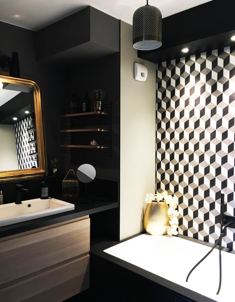 This is an example of a mid-sized scandinavian master wet room bathroom in Paris with a corner tub, white tile, gray tile, black tile, ceramic tile, black walls, an integrated sink, laminate benchtops, an open shower, flat-panel cabinets, light wood cabinets, light hardwood floors, brown floor and black benchtops.