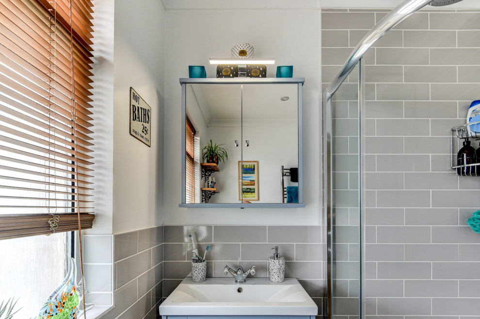 This is an example of a small traditional grey and white bathroom in Sussex with shaker cabinets, blue cabinets, a corner shower, a two-piece toilet, beige tiles, ceramic tiles, white walls, a built-in sink, brown floors, a sliding door, feature lighting, a single sink and a freestanding vanity unit.