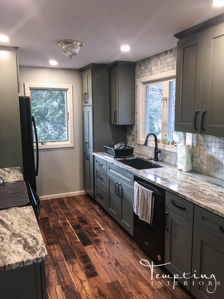 Photo of a small country galley kitchen in Boston with a drop-in sink, shaker cabinets, green cabinets, granite benchtops, white splashback, marble splashback, black appliances, light hardwood floors, brown floor and multi-coloured benchtop.