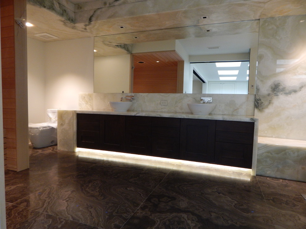 This is an example of an expansive modern bathroom in Los Angeles with shaker cabinets, dark wood cabinets, onyx benchtops, an open shower and marble floors.