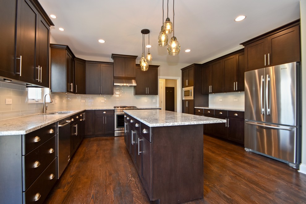 Open concept kitchen - large transitional u-shaped dark wood floor open concept kitchen idea in Chicago with recessed-panel cabinets, dark wood cabinets, white backsplash, glass tile backsplash, stainless steel appliances, an island and a double-bowl sink