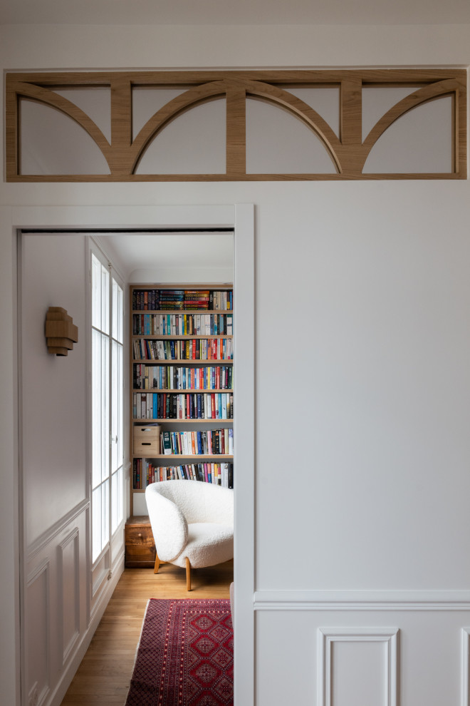 This is an example of a mid-sized scandinavian living room in Paris with a library, white walls, light hardwood floors and decorative wall panelling.