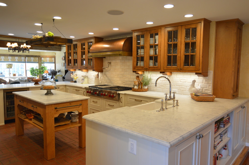 Photo of a large country u-shaped eat-in kitchen in DC Metro with a farmhouse sink, beaded inset cabinets, brown cabinets, marble benchtops, white splashback, ceramic splashback, stainless steel appliances, brick floors, with island and red floor.
