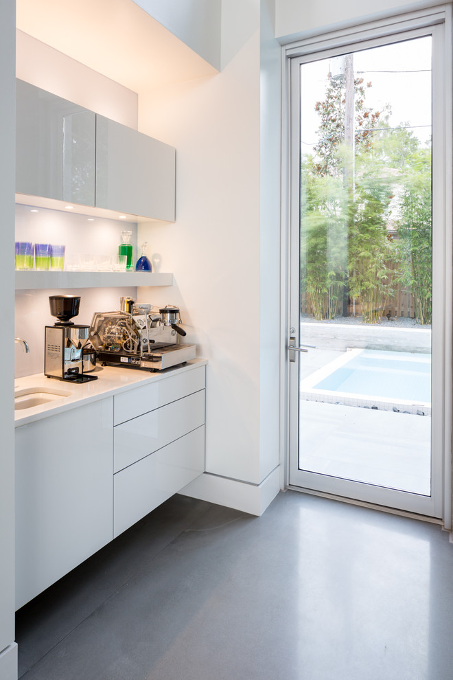 This is an example of a mid-sized modern single-wall wet bar in Orlando with an undermount sink, flat-panel cabinets, white cabinets, quartz benchtops, blue splashback, glass sheet splashback and concrete floors.