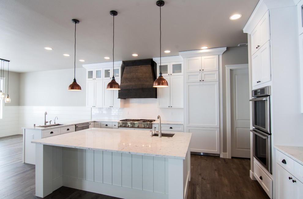 Design ideas for a large country u-shaped open plan kitchen in Seattle with an undermount sink, shaker cabinets, white cabinets, quartz benchtops, white splashback, ceramic splashback, stainless steel appliances, with island, dark hardwood floors and brown floor.