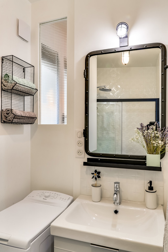 Photo of a small midcentury 3/4 bathroom in Paris with a curbless shower, a wall-mount toilet, white tile, ceramic tile, white walls, ceramic floors, an integrated sink, tile benchtops, multi-coloured floor and a sliding shower screen.