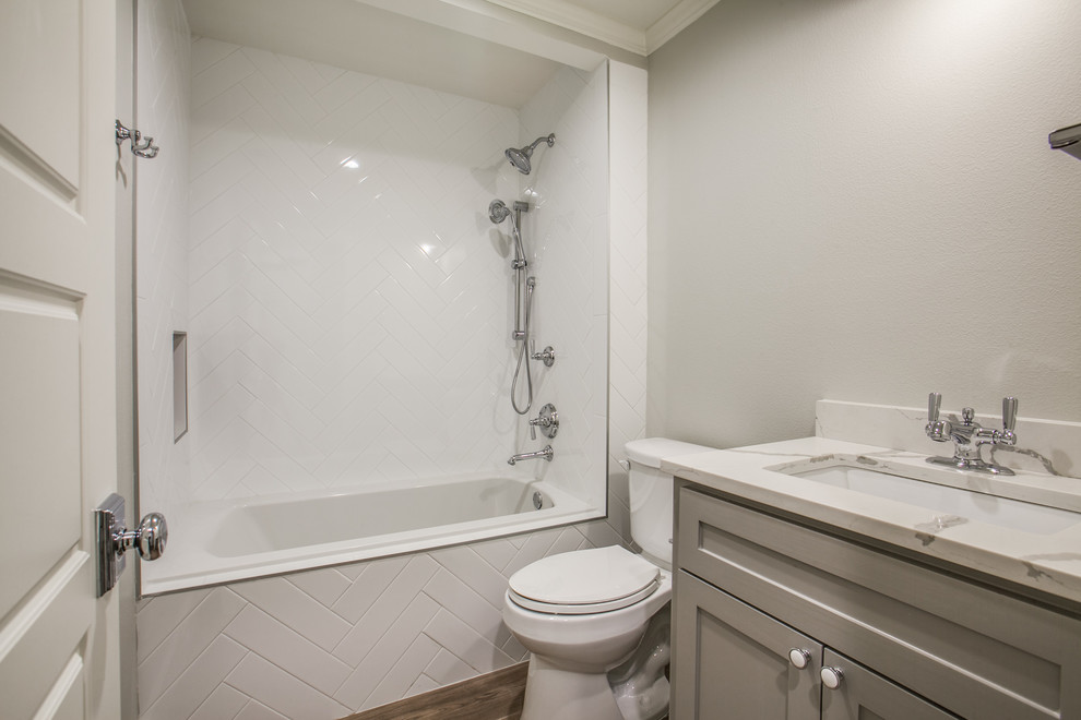 This is an example of a mid-sized arts and crafts kids bathroom in Dallas with shaker cabinets, grey cabinets, a drop-in tub, a shower/bathtub combo, a two-piece toilet, black tile, ceramic tile, grey walls, mosaic tile floors, an undermount sink and engineered quartz benchtops.