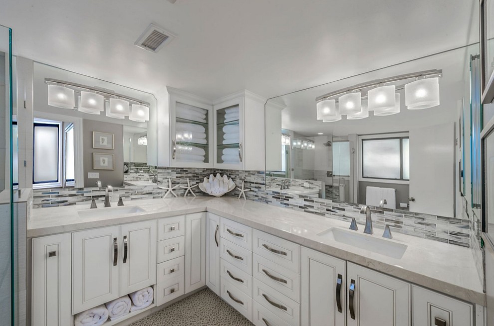 This is an example of a large beach style master bathroom in San Diego with beaded inset cabinets, white cabinets, matchstick tile, marble benchtops, a corner shower, grey walls, pebble tile floors, an undermount sink, beige floor and a hinged shower door.