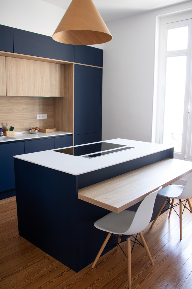 Immagine di una cucina contemporanea chiusa con lavello integrato, ante blu, top in superficie solida, paraspruzzi in legno, elettrodomestici in acciaio inossidabile, parquet chiaro e top bianco