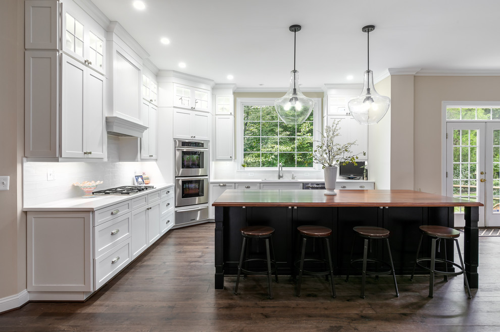 Huge transitional l-shaped dark wood floor and brown floor eat-in kitchen photo in DC Metro with an undermount sink, shaker cabinets, white cabinets, wood countertops, white backsplash, ceramic backsplash, stainless steel appliances, an island and brown countertops