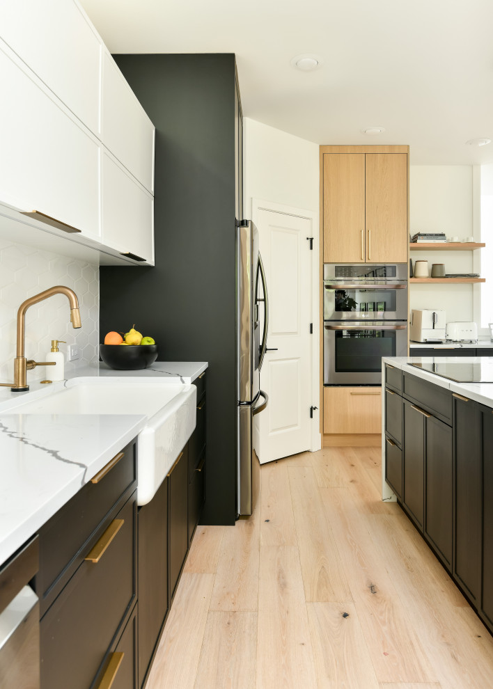 This is an example of a large modern single-wall eat-in kitchen in Seattle with a farmhouse sink, shaker cabinets, black cabinets, quartz benchtops, white splashback, porcelain splashback, stainless steel appliances, medium hardwood floors, with island, yellow floor and white benchtop.