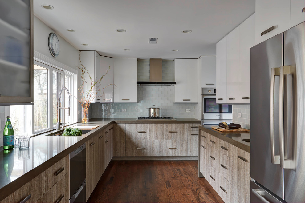 Large elegant u-shaped medium tone wood floor and brown floor enclosed kitchen photo with a double-bowl sink, flat-panel cabinets, distressed cabinets, solid surface countertops, white backsplash, glass tile backsplash, stainless steel appliances and no island