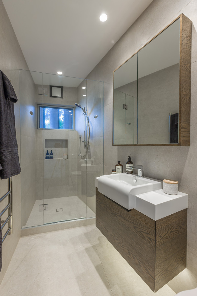 Example of a mid-sized trendy 3/4 beige tile and ceramic tile ceramic tile, beige floor and single-sink alcove shower design in Auckland with flat-panel cabinets, dark wood cabinets, a one-piece toilet, beige walls, a wall-mount sink, wood countertops, a hinged shower door, brown countertops and a built-in vanity