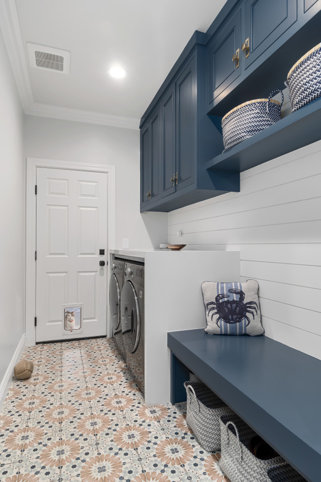 This is an example of a mid-sized beach style single-wall dedicated laundry room in Orange County with recessed-panel cabinets, blue cabinets, granite benchtops, white walls, ceramic floors, a side-by-side washer and dryer, multi-coloured floor and white benchtop.
