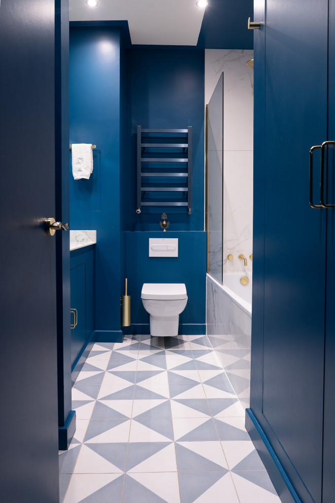 На фото: главная ванная комната среднего размера в стиле модернизм с синими фасадами, полновстраиваемой ванной, инсталляцией, белой плиткой, мраморной плиткой, синими стенами, полом из цементной плитки, раковиной с несколькими смесителями, разноцветным полом, тумбой под одну раковину и встроенной тумбой с