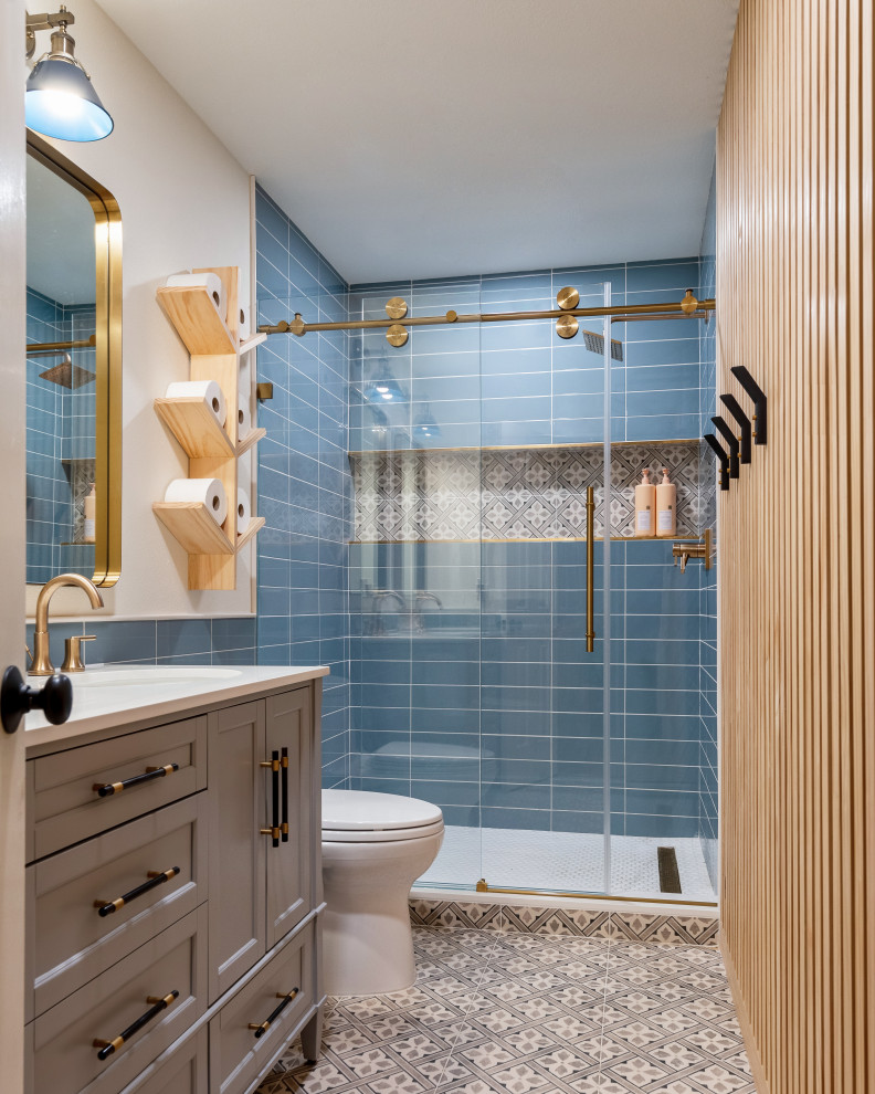 This is an example of a transitional 3/4 bathroom in Houston with recessed-panel cabinets, grey cabinets, an alcove shower, blue tile, white walls, an undermount sink, engineered quartz benchtops, multi-coloured floor, a sliding shower screen, white benchtops, a single vanity, a built-in vanity and wood walls.
