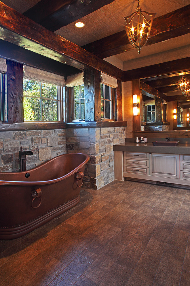 This is an example of a large country master bathroom in Minneapolis with raised-panel cabinets, beige cabinets, a freestanding tub, beige tile, stone tile, beige walls, dark hardwood floors and a vessel sink.