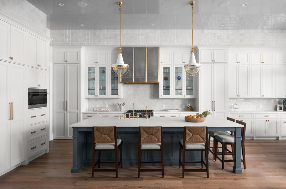 Design ideas for a beach style kitchen in Jacksonville with a farmhouse sink, shaker cabinets, white cabinets, white splashback, stainless steel appliances, medium hardwood floors, with island and white benchtop.