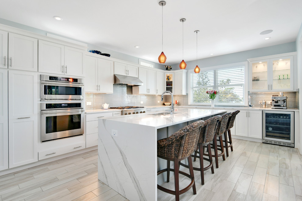 Inspiration for a mid-sized transitional u-shaped porcelain tile and gray floor open concept kitchen remodel in Tampa with a double-bowl sink, recessed-panel cabinets, white cabinets, marble countertops, gray backsplash, cement tile backsplash, stainless steel appliances and an island