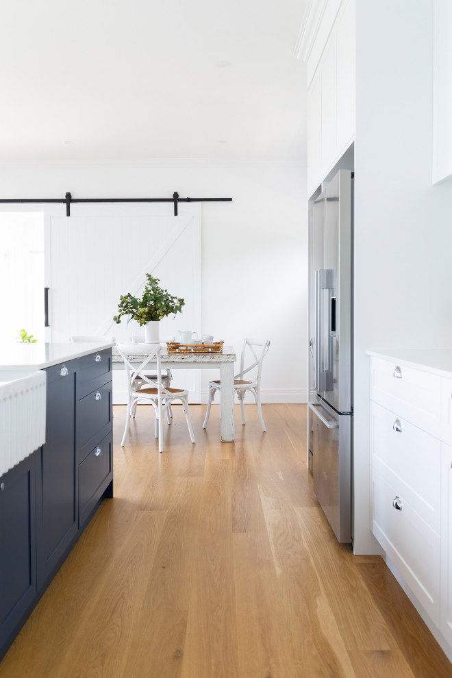 Design ideas for a traditional galley kitchen in Canberra - Queanbeyan with a farmhouse sink, shaker cabinets, blue cabinets, quartz benchtops, white splashback, subway tile splashback, stainless steel appliances, light hardwood floors, with island and white benchtop.