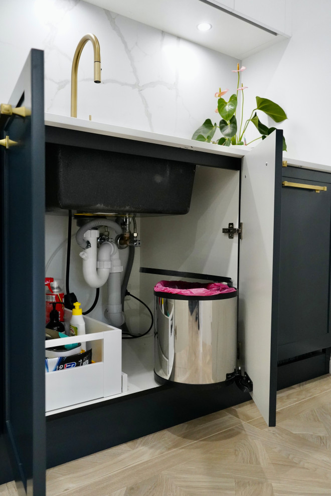 Inspiration for a large transitional galley open plan kitchen in Sydney with an undermount sink, shaker cabinets, black cabinets, quartz benchtops, white splashback, engineered quartz splashback, black appliances, light hardwood floors, with island, brown floor and white benchtop.