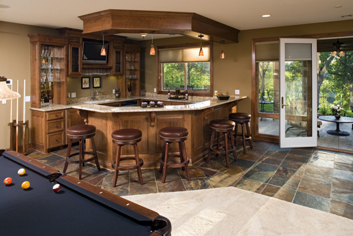 Photo of a large traditional seated home bar in Minneapolis with an undermount sink, medium wood cabinets, granite benchtops, ceramic floors and recessed-panel cabinets.